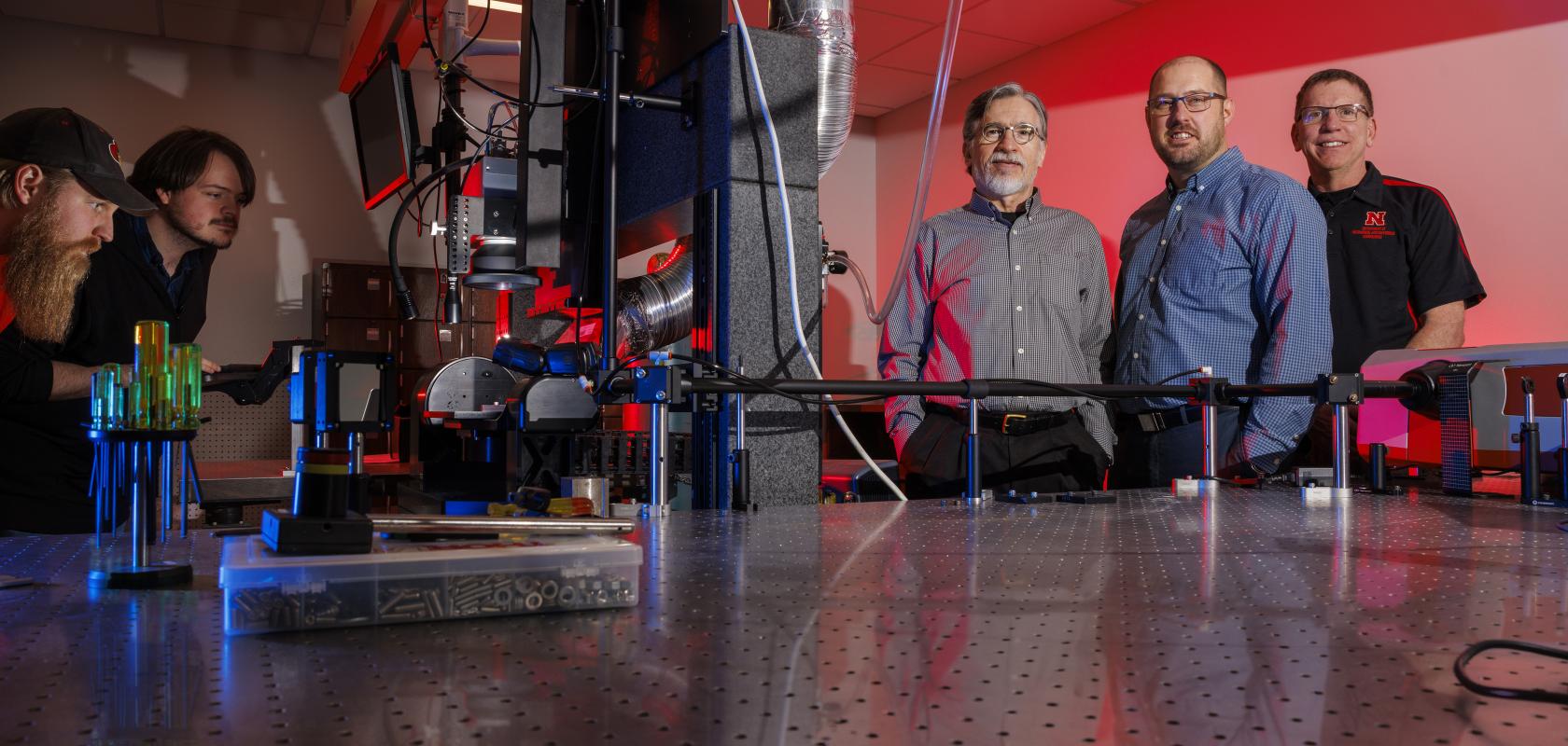 Researchers stand around a light table at the Center for Electro-optics and Functionalized Surfaces, University of Nebraska-Lincoln
