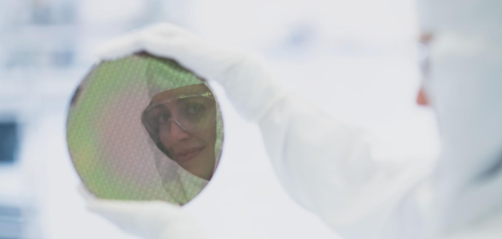 A cleanroom worker holds up an integrated circuit wafer