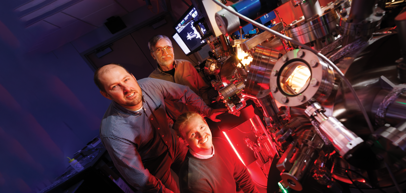Craig Zuhlke (left), George Gogos (back) and doctoral student Graham Kaufman (front), pose with a Leybold ultra-high vacuum laser surface processing and materials analysis system